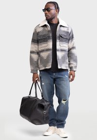 Giacca di lana grigia e bianca con collo in pelliccia shearling, t-shirt nera, jeans in denim strappati e borsa a tracolla in pelle nera.