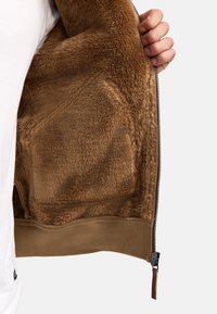 Brun fleece-foret inderside med en glat tekstur, med en lynlås og en kontrasterende stofkant forneden.
