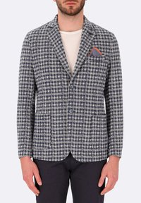 Blazer a scacchi bianco e blu navy con due tasche frontali, rever a punta e fazzoletto rosso, con chiusura a due bottoni.