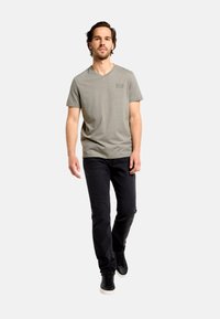 Šedé tričko s výstrihom do V a krátkymi rukávmi, kombinované s čiernymi džínsami a čiernymi teniskami. Jednoduchá látka s jemným logom na hrudi.