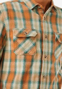 Camicia flanella a quadri in arancione, crema e teal. Presenta un'apertura con bottoni frontale e due tasche sul petto con patta, tessuto testurizzato e colletto classico.
