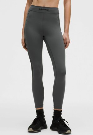 Leggings grises de cintura alta con un diseño ajustado, textura suave y costuras laterales. El logo de la marca es visible en la cinturilla elástica.