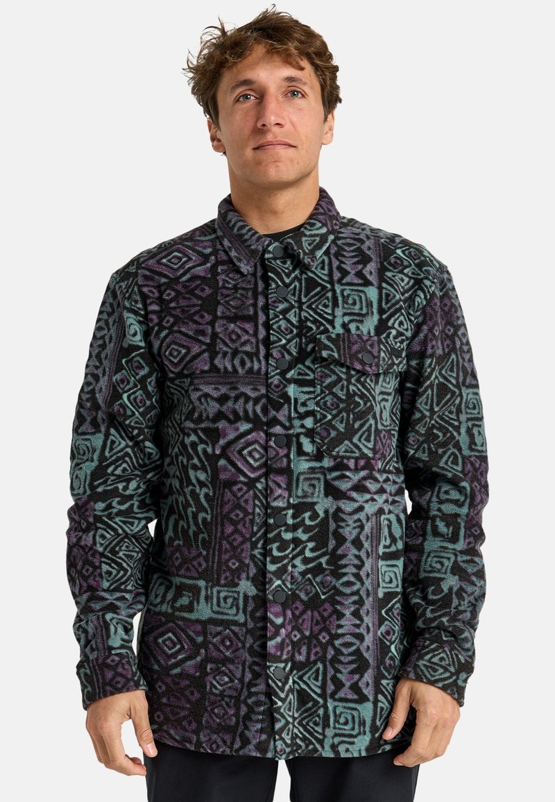 Camisa de forro polar en negro, verde azulado y púrpura con un patrón geométrico, que cuenta con un cierre de botones en el frente y un bolsillo en el lado izquierdo del pecho.