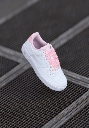 Tenisky Nike Air Force 1, biela koža s ružovými detailmi, s perforovanou špičkou, ružovými šnúrkami a polstrovaným golierom.