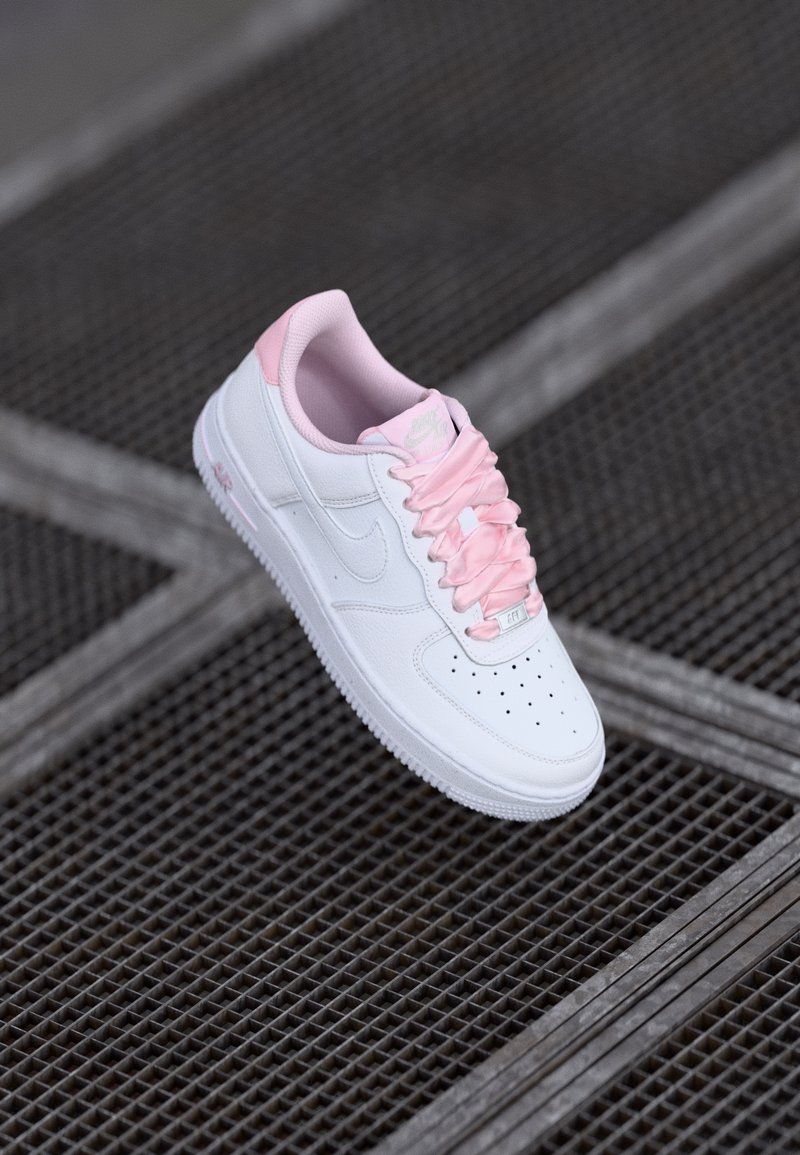 Sneakers Nike Air Force 1, in pelle bianca con dettagli rosa, presentano una punta forata, lacci rosa e colletto imbottito.
