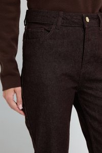 Mörkbruna jeans i denim med figursydd design, synlig söm, en framficka och en guldknäppning vid midjebandet. Texturerad yta.