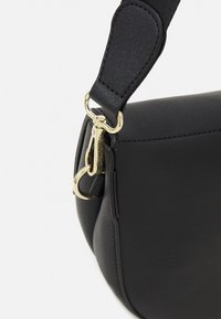 Borsa nera con un esterno in pelle liscia, forma curva e hardware dorato. Presenta una tracolla resistente con un moschettone per il fissaggio.