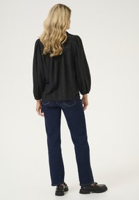 Melna plisēta blūze ar garām piedurknēm un noapaļotu kaklu, apvienota ar tumši ziliem taisnās kājas džinsiem un melniem masīviem mokasīniem.