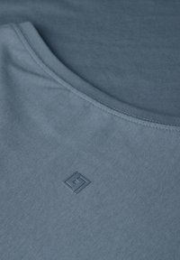 Canotta in cotone blu con scollo rotondo e un delicato dettaglio del logo. Il tessuto ha una consistenza liscia e un aspetto leggero.