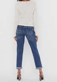 Maglione bianco lavorato a maglia con texture a coste e maniche lunghe abbinato a jeans di denim blu con risvolti, dotati di tasche posteriori e vestibilità comoda.