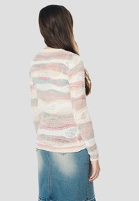 Kötött pulóver több színű, pasztell tónusú csíkokkal; hosszú ujjú, laza szabású és texturált mintázatú; farmer szoknyával párosítva.