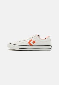 Zapatilla de lona blanca con logo de estrella naranja y detalle de chevrón, suela de goma negra y acento rojo contrastante en el collar.