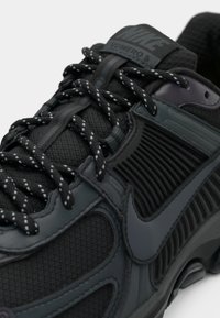 Sneaker Nike Vomero 5 nera con tomaia in mesh testurizzato, dettagli in gomma, lacci riflettenti e design della suola ammortizzata.