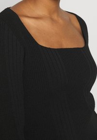 Haut noir à côtes avec un décolleté carré. Le tissu est texturé, avec des lignes verticales et une silhouette ajustée.