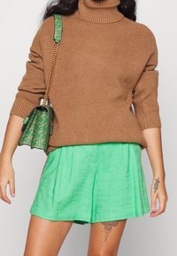 Brun randig polotröja kombinerad med ljusgröna texturerade shorts. Modellen bär en liten grön mönstrad handväska med kedjestropp.