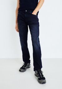 Jeans blu scuro con una vestibilità slim, design a cinque tasche e una leggera scoloritura. Abbinati a sneakers nere e grigie. Texture del denim liscia.
