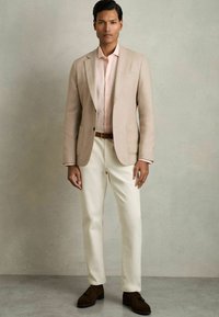 Blazer bej peste o cămașă roz deschis, pantaloni crem și pantofi maro închis. Design simplu, croi adaptat, texturi netede și culori subtile.