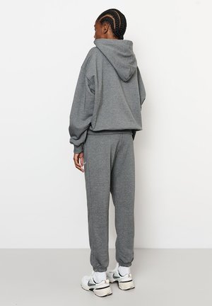 Szara bluza z kapturem, luźnym krojem i długimi rękawami; dopasowane szare spodnie dresowe z elastycznymi mankietami i bocznymi kieszeniami; białe tenisówki.