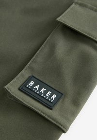 Olivově zelená látka s hladkou texturou; obsahuje černou obdélníkovou nálepku, na které je výrazně napsáno "BAKER by TED BAKER".