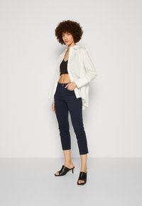 Biely košeľový top, čierny crop top, námornícke skrátené nohavice a čierne otvorené podpätky. Hladká tkanina, štruktúrovaný dizajn, ležérny strih.