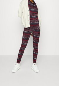 Dvoudílný outfit skládající se z vzorovaného topu a legín v námořnické modré, červené a bílé s vánočními motivy. Doplněno krémovým kardiganem a bílými teniskami.