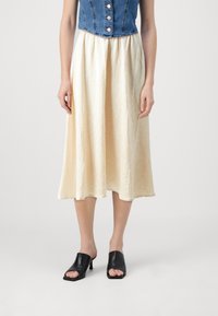 Denim kort vest med knapper, kremfarget midi-skjørt med krøllete tekstur, og svarte hevede mules med åpen tå.