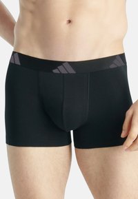 Svarta boxerkalsonger med en mjuk, elastisk midja som har tre grå ränder. Slät textur, åtsittande form och inga ytterligare mönster.