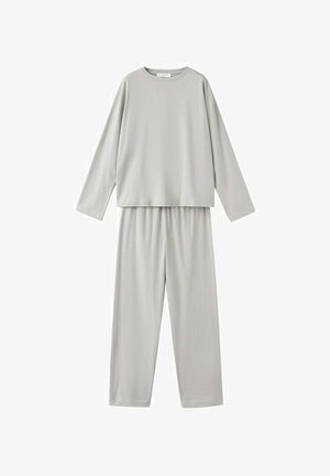 Femme en haut court à manches longues gris clair et pantalon assorti à cordon, regardant vers le bas avec les mains derrière le dos.