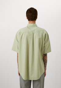 T-shirt met korte mouwen in lichtgroen met een gestreept patroon, achterkant met plooidetail en een standaard kraag, gedragen over een grijze broek.
