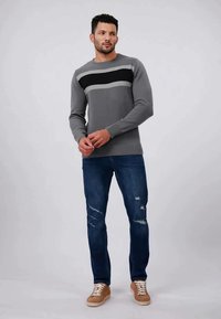 Grijze gebreide trui met zwarte en lichtgrijze strepen, gecombineerd met versleten blauwe jeans en beige sneakers. Geweven stof en ribbelmanchetten.