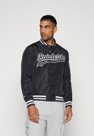 Chaqueta bomber de satén negra con letras blancas, puños a rayas y cierre de botones. Presenta bordados de "Raiders" y "Desde 1960".