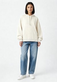 Sweat à capuche de couleur crème avec une poche avant et des poignets côtelés, associé à un jean large bleu clair et des baskets blanches.