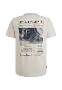 Beige bavlněné tričko s kulatým výstřihem a krátkými rukávy. Na zadní straně má grafický potisk, který zahrnuje text o letadlech a dobrodružstvích.