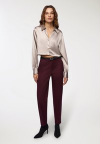Jedwabna bluzka w jasnoszarym kolorze z kołnierzykiem i guzikami, połączona z głęboko burgundowymi spodniami o kroju tailor i czarnymi wysokimi botkami.