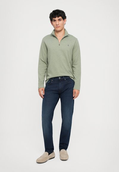 Φωτεινό πράσινο πουκάμισο με μακριά μανίκια και φερμουάρ τετάρτου, συνδυασμένο με σκούρα μπλε τζιν και μπεζ μοκασίνια. Απαλή υφή, άνετη εφαρμογή, μίνιμαλ σχεδίαση.