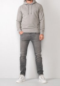Sudadera gris con cordones y un bolsillo canguro, combinada con jeans gris ajustados y zapatillas blancas. Diseño y textura simples y casuales.