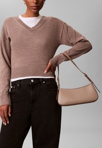 Maglione marrone lavorato a maglia con scollo a V, abbinato a jeans neri a vita alta. Una borsa beige chiaro con motivo e tracolla completa il look.