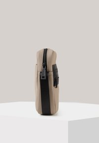 Borsa beige con una superficie liscia, cerniera nera e tracolla. Design compatto con un accentuazione laterale per una maggiore funzionalità.