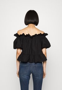 Schwarze schulterfreie Bluse mit Rüschensaum am Hals und an den Ärmeln, mit einem Peplum-Saum. Getragen mit blauen Jeans. Aus glattem Baumwollstoff.