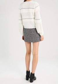 Tjock vit stickad tröja med grå ränder, kombinerad med en texturerad grå minikjol och svarta ankelstövlar, sedd bakifrån.