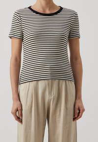 Top court à manches courtes rayé en écru et noir avec une texture côtelée, présentant un col rond et une silhouette ajustée, associé à un pantalon beige.