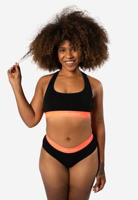 Zwarte sport-bh en bikini-onderstuk met een feloranje tailleband waarop "HAPPY SHORTS" in witte tekst staat. Zacht, rekbaar materiaal en een snug-fit.