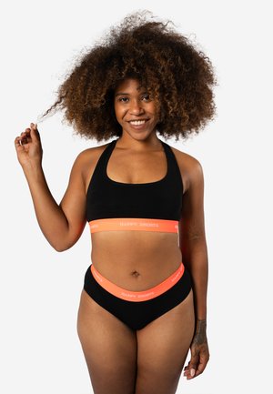Zwarte sport-bh en bikini-onderstuk met een feloranje tailleband waarop "HAPPY SHORTS" in witte tekst staat. Zacht, rekbaar materiaal en een snug-fit.