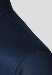 Granatowa koszula z gładkiego, błyszczącego materiału o delikatnym połysku, z wyraźnym kołnierzykiem i starannymi szwami wzdłuż krawędzi.