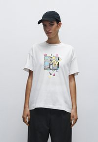 Vit bomull t-shirt med en färgglad MTV-logotyp i grafisk design med geometriska inslag. Rund halsringning och korta ärmar, kombinerad med mörka byxor.