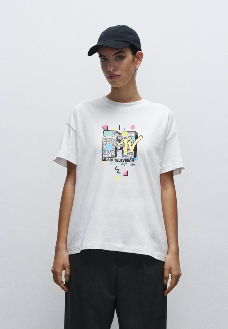 Vit bomull t-shirt med en färgglad MTV-logotyp i grafisk design med geometriska inslag. Rund halsringning och korta ärmar, kombinerad med mörka byxor.
