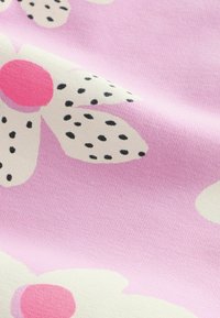 Tissu rose avec de grandes fleurs crème présentant des centres rose vif et des pois noirs sur les pétales.