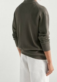 Khaki ribbed sweater with a polo collar, long sleeves, and fitted cuffs, paired with white pants, displayed from the back.