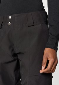 Μαύρο αδιάβροχο παντελόνι με μεταλλικούς κλείστρες, πλαϊνές τσέπες και κομψή, λεία υφή με εφαρμοστό λάστιχο στη μέση.