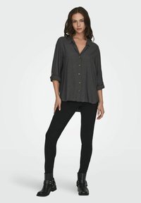 Dunkelgraues Hemd mit aufgerollten Ärmeln, kombiniert mit schwarzen Skinny-Jeans und schwarzen Ankle-Boots mit Schnalle. Glattes Material und lockere Passform.